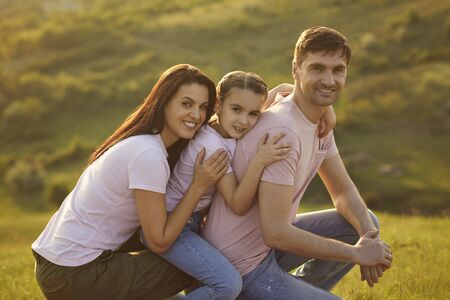 Portrait of a happy family looking at the camera on summer nature. Mother father and daughter on vacation outdoors in a park.の写真素材