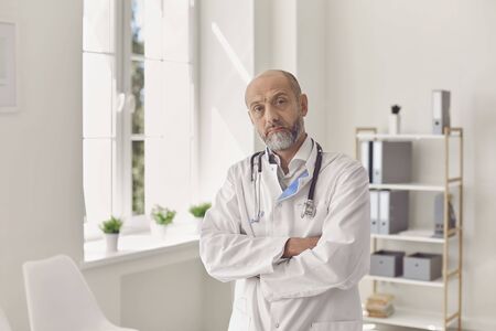 Portrait of serious, experienced senior age family doctor in his private practice office. Concept of medical expertise, health care service and regular physical check up.の写真素材