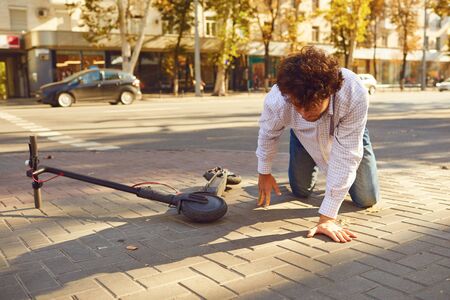 Accident with an electric scooter. A man fell from a scooter on a city street. Trauma in incident.の写真素材