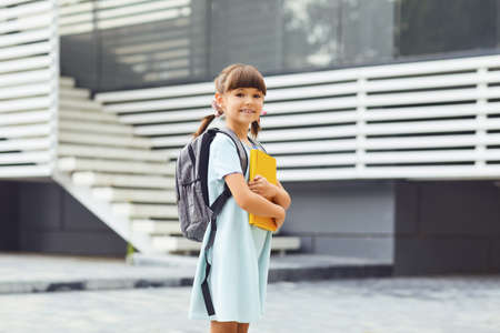 Schoolgirl with a backpack and books in hand goes to school.