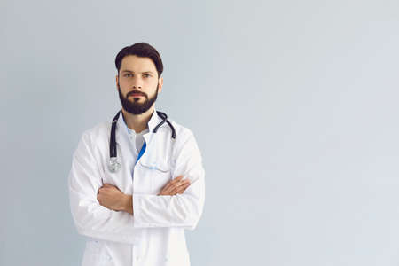 Serious medical doctor with crossed arms on grey background, copy space text. Young physician, pediatrician or nurse with stethoscope. Health care conceptの写真素材