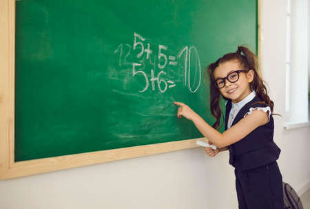 Back to school. A schoolgirl with glasses writes on a school board in a classroom at a lecture. Training education care parenting lessons training lecture for kids of students at school lyceum.の写真素材