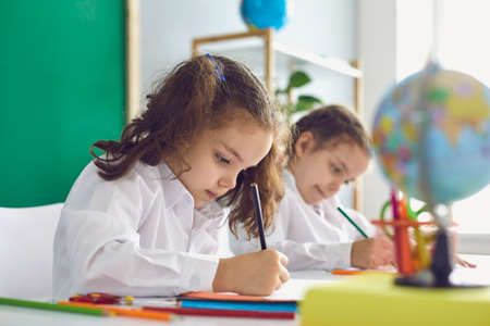 Back to school. Children schoolchildren write while sitting at the table in the classroom. Learning...