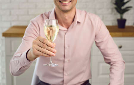 A glass of champagne in a man's hand. A young man holds a glass of wine looking at the camera on a laptop video conference monitor. Online communication remotely.の写真素材