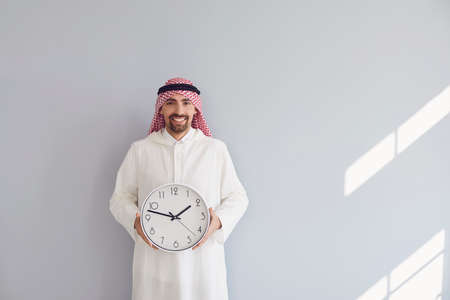 Handsome arab man holding a watch in his hands on a gray background.の写真素材
