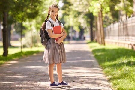 Back to school. Happy schoolgirl smiles while standing on the road to school in the morning. Education study school college university.の写真素材