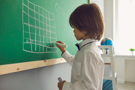 Chess lesson for children. Boy draws a chessboard on the green board in the classroom. Learning...