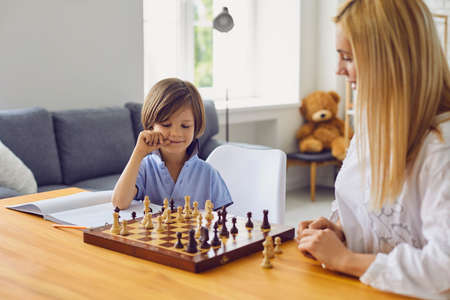 Family hobbies. Young mother playing chess with her son at home. Cute little boy engaged in board game with his parent in light roomの写真素材