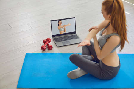 Online fitness concept. Young slender woman on the floor doing exercises, stretching, warm-up and uses a video fitness lesson. Young slender woman fitness instructor doing exercises online.の写真素材