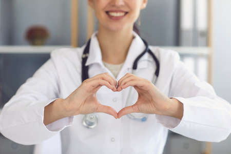 Unrecognizable female doctor showing heart gesture at clinic, closeup view. Cardiologist...