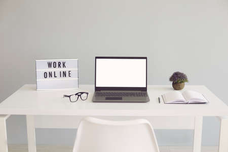 WORK ONLINE sign and laptop with blank screen on desk at home office, mockup for design. Freelancer...