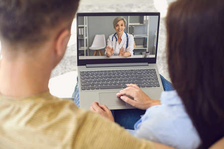 Online consultation with doctors. Couple has a video call with doctors using laptop in the room. Remote medical consultation.の写真素材