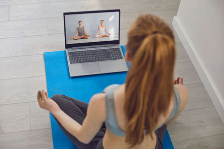 Yoga training online. Young fit girl on the floor home doing yoga in the lotus position uses a video...