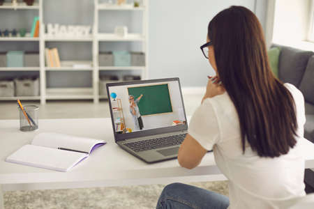 Online training. Girl student listens to the lecture of the teacher has video chat laptop sitting at...