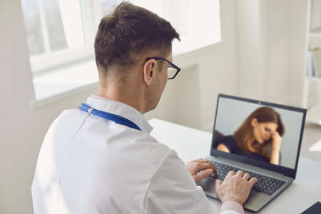 Doctor online.Telemedicine.Medical conference online.Man doctor uses a laptop and listens to a patient.A young woman patient uses a video call to a doctor.The patient has headache, weakness, depression.の写真素材