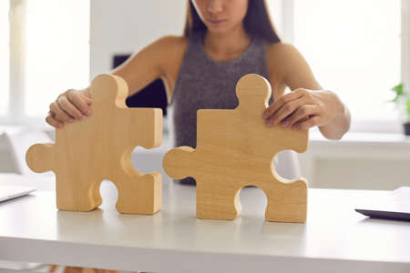 Business woman standing and trying to make whole picture from wooden details puzzle alone in office, selective focus. Leadership, successful management and strategy conceptの写真素材