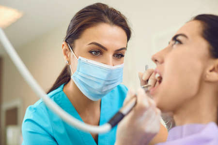 Young woman doctor dentist in medical mask making professional curing of tooth for woman patient in dental clinic. Dental care and visiting dentist conceptの写真素材