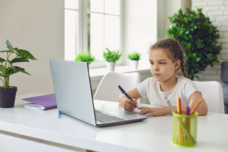 Online schooling. Cute little girl participating in video lesson on laptop computer at home. Child...