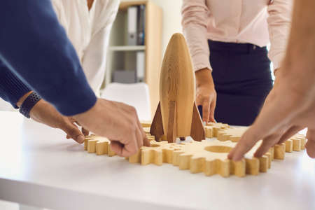 Businesspeople at office table with rocket and cogwheels as metaphor of company team working on new strategy. Entrepreneurs developing start-up idea, starting business, using innovative work methodsの写真素材