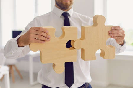 Cropped businessman or company manager joining 2 pieces of jigsaw puzzle. Metaphor for finding business solution or missing link, building strong business, implementing effective work methodsの写真素材