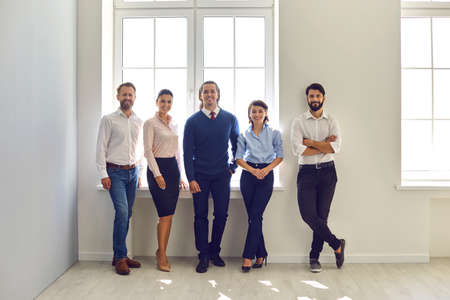 Friendly company staff gathered together for corporate meeting. Group portrait of happy smiling office workers. Team of confident business professionals looking at camera standing in modern officeの写真素材