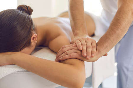Closeup of relaxed woman getting medical body massage done by professional massagist or physiotherapist in modern clinic. Masseur helping female patient reduce pain and relax musclesの写真素材
