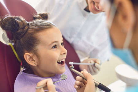 Little brave smiling little girl getting tooth cavity from dentist and assistant in dental clinic...