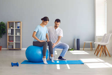 Man doctor chiropractor or osteopath fixing woman on fitness ball in right position for pain relief...