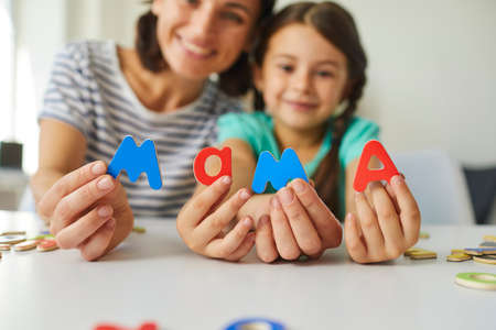 Smiling mommy and preschool daughter make word Mama playing with ABCs, closeup in soft focus of...