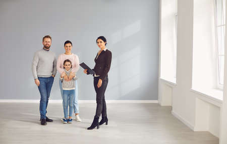 Real estate agent woman smiling with clipboard and family in new home.の写真素材