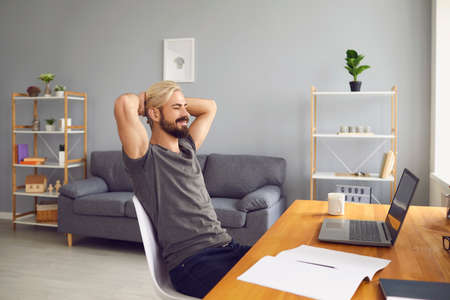 Young man sitting at home, looking at laptop screen and smiling during online meeting, videocall,...