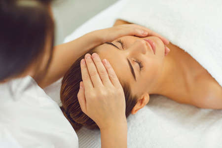 Close-up of positive womans face recieving procedure of professional manual relaxing massage from masseur in beauty spa salon, top and rear view. Rejuvenating facial massage in cosmetologyの写真素材