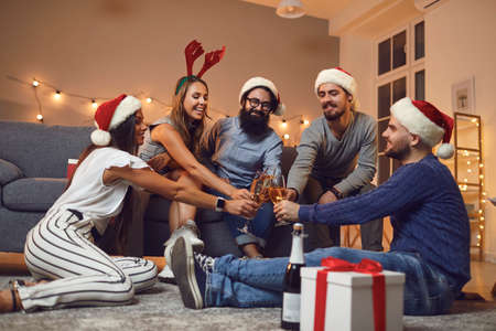 Group of young happy friends sitting on floor and drinking champagne during Christmas holiday festive party at home. Christmas, New year, birthday, corporate party celebrationの写真素材