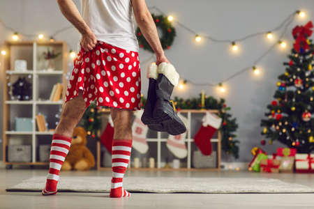 Drunk man who lost his Santa Claus costume comes home in the morning after partying hard all Christmas night feeling guilty and exhausted wearing red and white striped socks and polka dot boxer shortsの写真素材