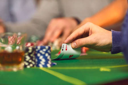 Closeup of hand rasing a pair of aces on green baize card table with stacks of chips and drinks....