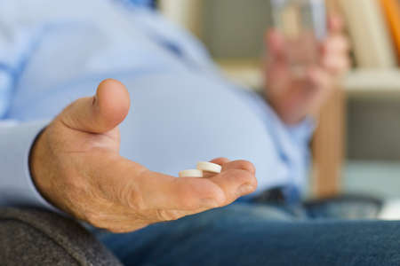 Healthcare and medication. Closeup of senior mans hand holding two medical pills. Mature male taking medicine for easing pain, controlling blood sugar, lowering blood pressure, or curing infectionの写真素材