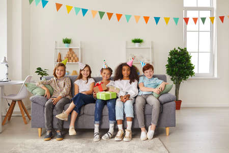 Bunch of happy diverse children and birthday girl holding presents, all wearing funny party hats,...