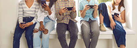 Cropped shot of children immersed in mobile devices. Kids sitting on windowsill and ignoring real...
