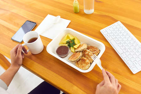 Hands of office worker eating healthy balanced meal from container delivered by food delivery...