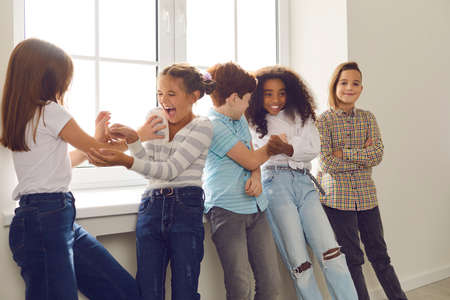 Active group of multiethnic children have fun together and tickle each other standing by a large window in a bright room. Concept of positive emotions.の写真素材