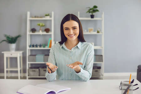 Young smiling woman sitting at home, looking at camera and explaining something with hands during...