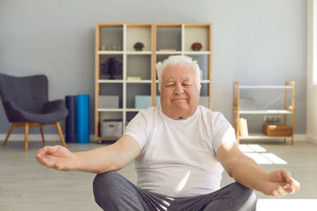 Happy relaxed chubby mature man practising Easy or Lotus yoga pose, meditating and doing hatha...