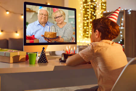 Smiling grandparents with birthday cake congratulating grandson with birthday online from laptop...