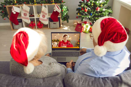 Self-isolation, staying at home on Christmas holidays, virtual family meeting in quarantine. Grandparents in Santa caps video calling their happy grandson. Over shoulder view of laptop screenの写真素材