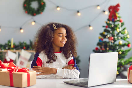 Schoolgirl stays home for Christmas holidays. African American 8-10 year old girl looking at laptop computer screen having video call with friends or relatives or watching a Xmas movieの写真素材
