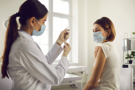 Vaccination and immunization concept. Hospital nurse drawing medication out of vial before giving injection to patient. Young woman getting Covid-19 or flu antiviral vaccine at the doctors officeの写真素材