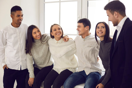 Discussion of training. Group of cheerful multiracial students are sitting on the windowsill and talking to each other. Concept of education, friendship, unity and a fun phase of life.の写真素材
