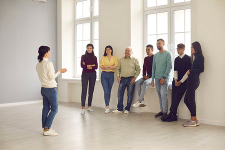 Speaker giving presentation to audience. Group of happy smiling diverse people standing in creative meeting space and listening to an interesting lecture by professional lifestyle or business coachの写真素材