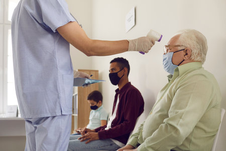 Cropped shot of medical worker measuring senior patients body temperature with non-contact digital...