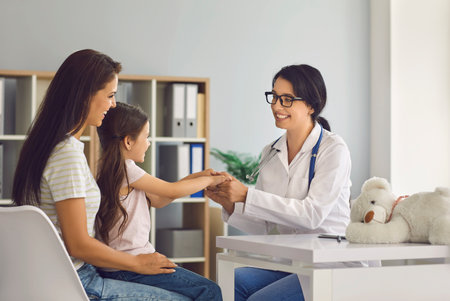 Female doctor smiling at patients in clinic office. Medical consultation for children. Children pediatrician doctor speaks with little girl and mother.の写真素材